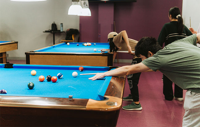 Student playing pool, aiming to hit the white ball on pool table